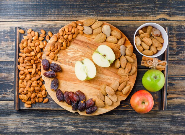 Manzanas y rodajas en una tabla de cortar con palitos de canela, fechas y almendras vista superior en pieza de madera y madera