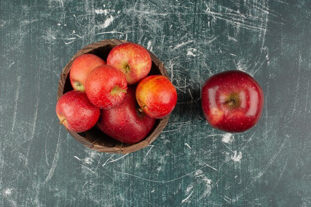 Manzanas rojas en balde sobre mesa de mármol.