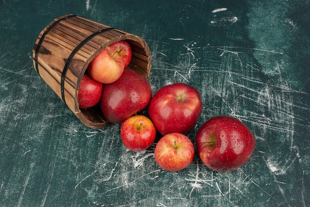 Manzanas rojas cayendo del balde sobre la mesa de mármol.