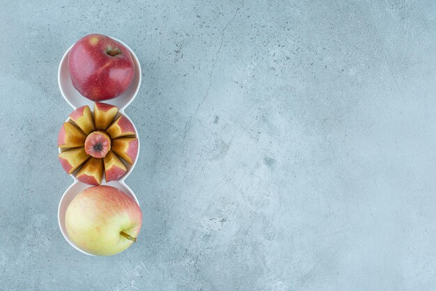 Manzanas rojas enteras y en rodajas en tazas blancas.