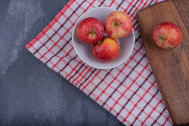 Manzanas rojas frescas en un tazón blanco con mantel.