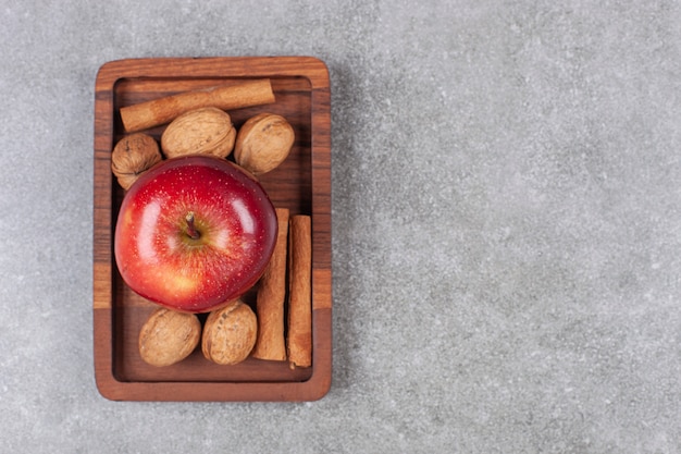 Manzanas rojas, nueces y ramitas de canela en placa de madera