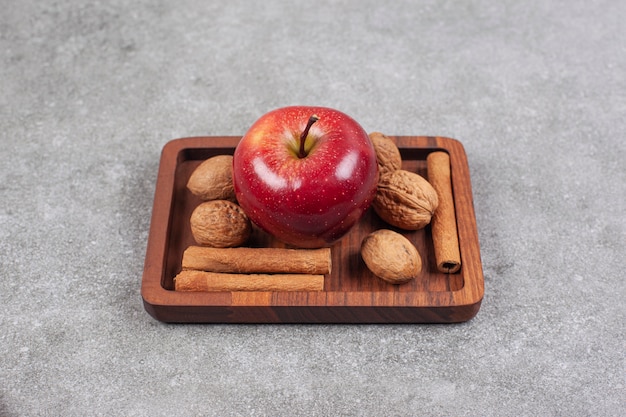 Manzanas rojas, nueces y ramitas de canela en placa de madera