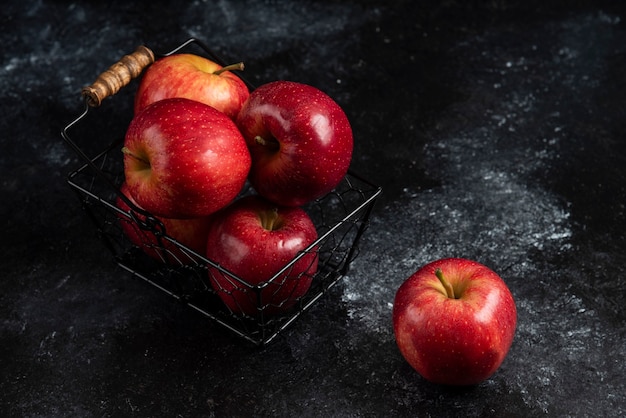 Manzanas rojas orgánicas maduras en canasta de metal sobre superficie negra. .