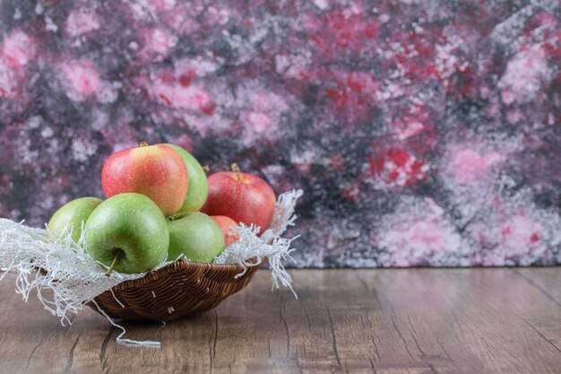 Manzanas rojas y verdes en una canasta de madera sobre la mesa.