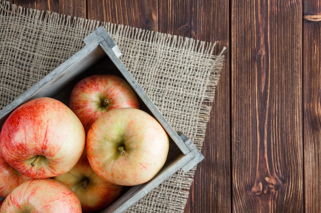 Manzanas rojas en una vista superior de la caja de madera sobre una tela de saco y espacio de fondo de madera para texto