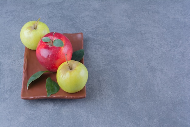 Manzanas sabrosas con hojas en placa de madera sobre la superficie oscura