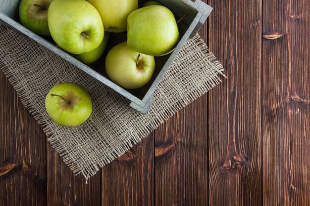 Manzanas verdes en una caja de madera plana yacía sobre una tela de saco y fondo de madera