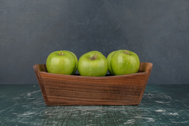 Manzanas verdes en caja de madera sobre superficie de mármol.