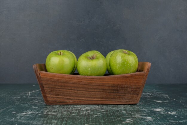 Manzanas verdes en caja de madera sobre superficie de mármol.