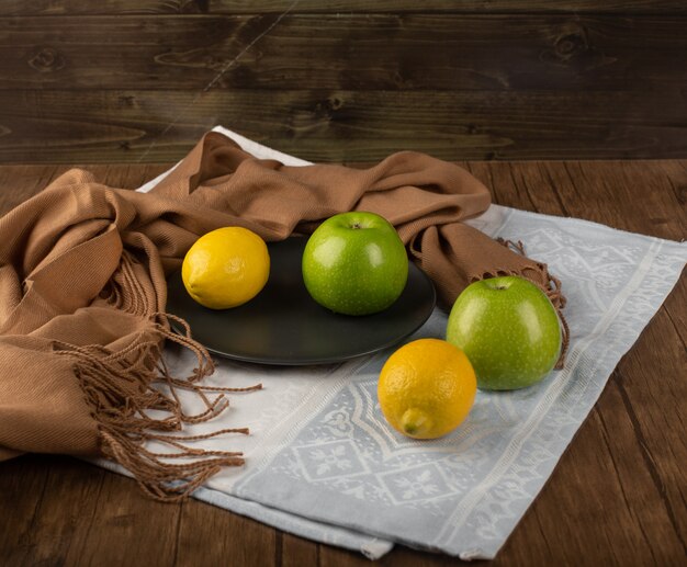 Manzanas verdes enteras y un limón en un plato negro sobre una toalla blanca