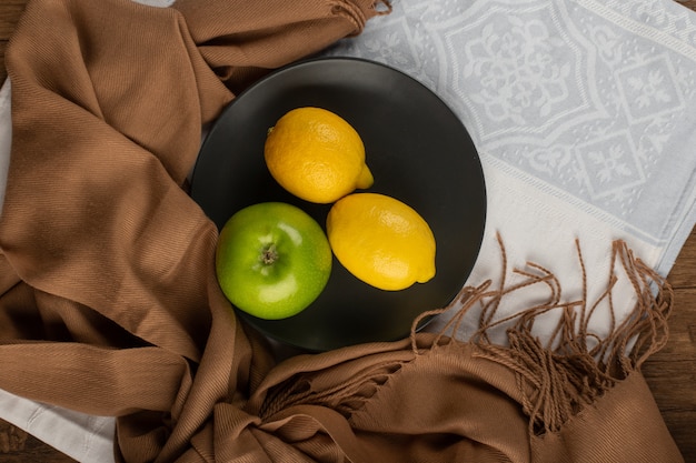 Manzanas verdes enteras y un limón en un plato negro.