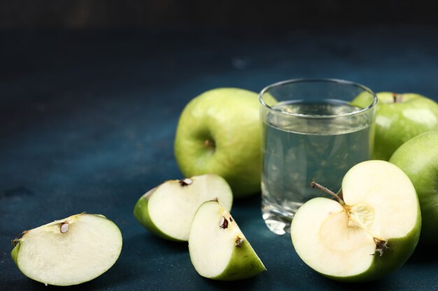 Manzanas verdes enteras y en rodajas con un vaso de jugo de manzana.