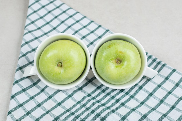 Manzanas verdes enteras en tazas blancas con mantel
