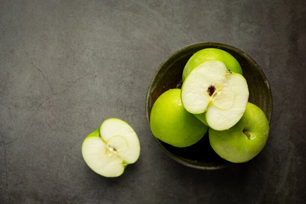 Manzanas verdes frescas cortadas por la mitad en un tazón negro sobre fondo oscuro