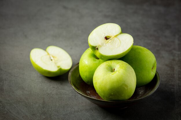 Manzanas verdes frescas cortadas por la mitad en un tazón negro sobre fondo oscuro