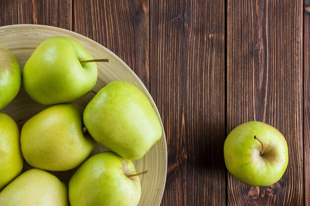 Manzanas verdes en un plato y alrededor de la vista superior en un espacio de fondo de madera para texto