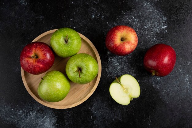 Manzanas verdes y rojas enteras y en rodajas en placa de madera.