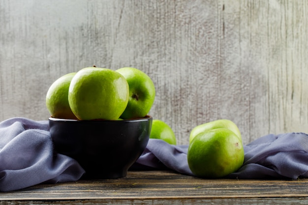 Manzanas verdes con textiles en un recipiente sobre fondo de madera y grunge