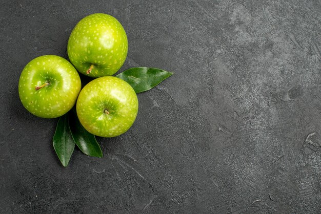 Manzanas verdes tres manzanas verdes con hojas sobre la mesa oscura