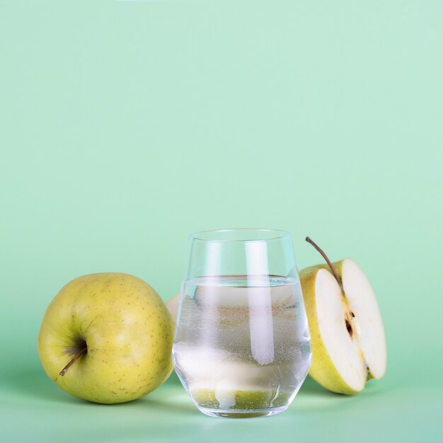 Manzanas verdes y vaso de agua sobre fondo verde