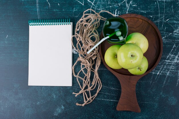 Foto gratuita manzanas verdes con un vaso de jugo en un rústico con un cuaderno a un lado.