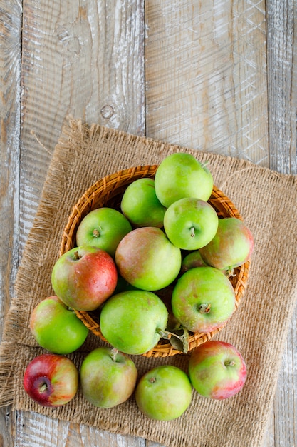 Foto gratuita manzanas en una vista superior de la cesta de mimbre en madera y un pedazo de saco