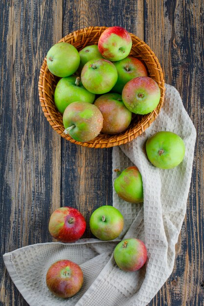 Manzanas en una vista superior de la cesta de mimbre sobre fondo de toalla de cocina y madera