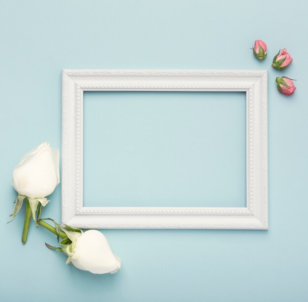 Maqueta marco vacío horizontal blanco con capullos de rosa sobre fondo azul.