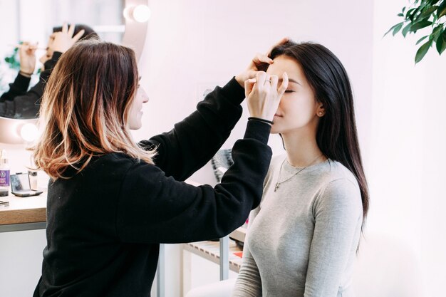 El maquillador hace las cejas de la señora que se sientan antes de ella