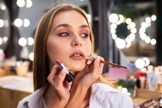 Maquilladora aplicando lápiz labial en labios de mujer sonriente con pincel