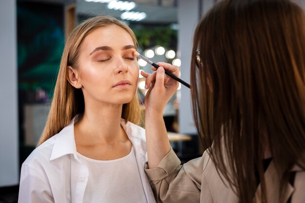 Maquilladora aplicando sombra de ojos en la cara con pincel