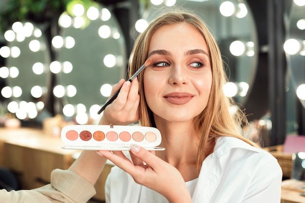 Maquilladora aplicando sombra de ojos en la cara con pincel