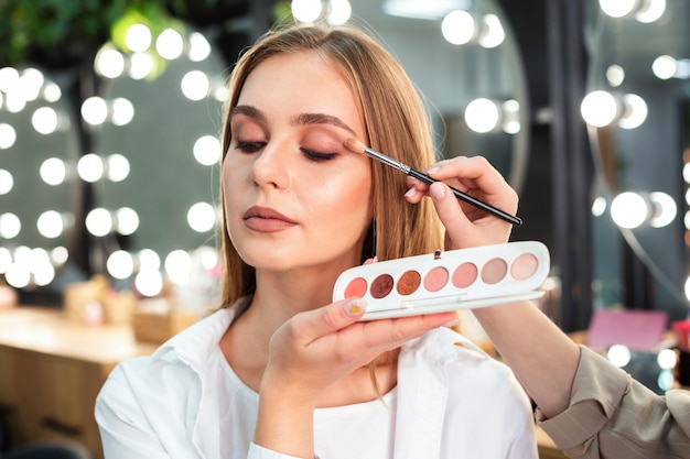 Maquilladora aplicando sombra de ojos a mujer con pincel