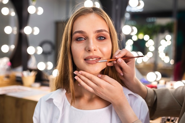 Maquilladora aplicar lápiz labial en mujer sonriente con pincel