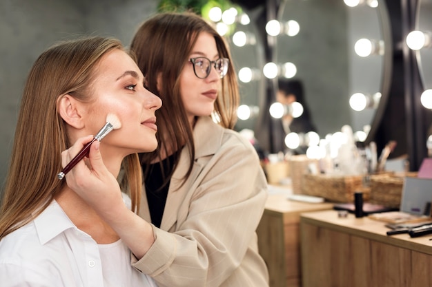 Maquilladora y mujer mirando al espejo aplicando contornos