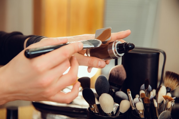 Maquilladora profesional que trabaja en el salón. El hombre de la profesion femenina. Concepto de igualdad de género. Manos masculinas con primer plano de cepillo