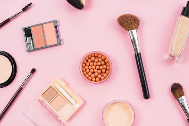 Maquillaje y arreglo de accesorios cosméticos sobre fondo rosa.