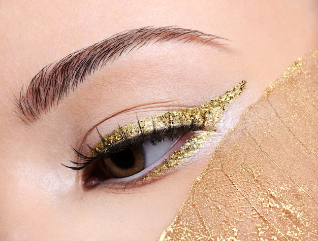 Foto gratuita maquillaje de moda en flecha delineador de ojos dorado en la mujer con una hoja amarilla