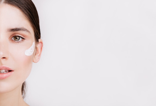 Sin maquillaje ni filtros. Foto de media cara de mujer sana de ojos verdes con crema en la piel.