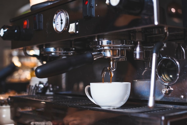 Máquina de café vierte el café recién en la taza blanca