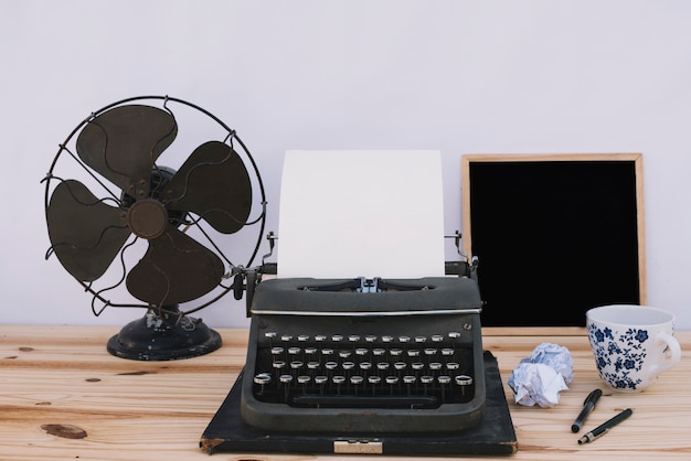 Máquina de escribir cerca de pizarra y ventilador