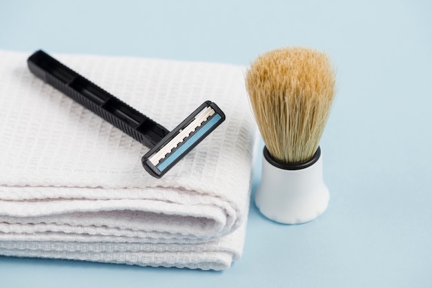 Maquinilla de afeitar en servilleta blanca doblada y brocha de afeitar clásica contra el fondo azul