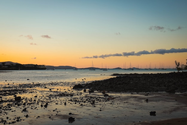 Mar con barcos en él rodeado por la playa y las colinas durante la puesta de sol por la noche