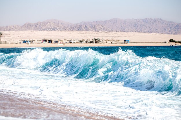 Mar embravecido con olas espumosas en tiempo soleado. Vista de la costa con montañas.