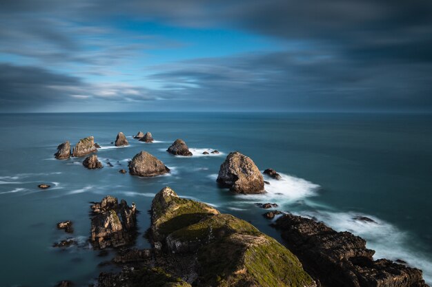 Mar con grandes rocas en el agua bajo un cielo nublado azul