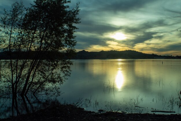 Mar rodeado de colinas bajo la luz del sol y un cielo nublado por la noche