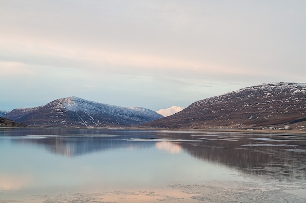 Mar rodeado de rocas cubiertas de nieve y reflejándose en el agua en Islandia