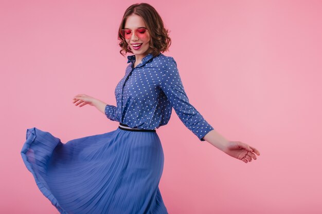 Maravillosa chica europea bailando con sonrisa inspirada. Retrato interior de mujer atractiva en falda larga azul.