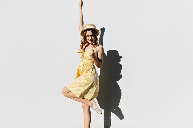 Maravillosa chica en traje vintage de pie sobre una pierna. Mujer rizada alegre en ropa amarilla bailando en un día soleado.